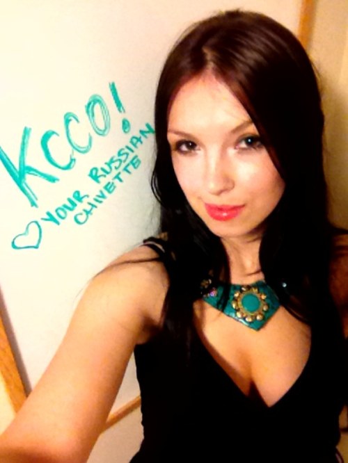 Pretty brunette with perky boobs takes selfie in cleavage showing black top next to KCCO written on white chalkboard