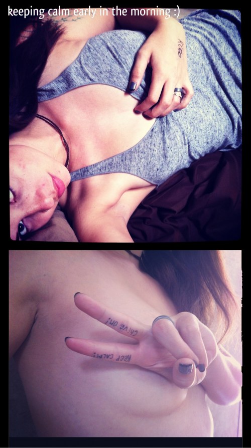 Brunette with Chive On written on fingers, perky boobs, and red lips takes selfie topless and on bed in bluish gray top