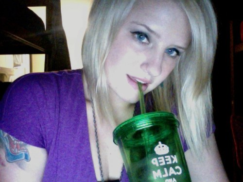 Pretty tattooed light-eyed blonde drinks juicy from green KCCO glass and takes selfie in purple top