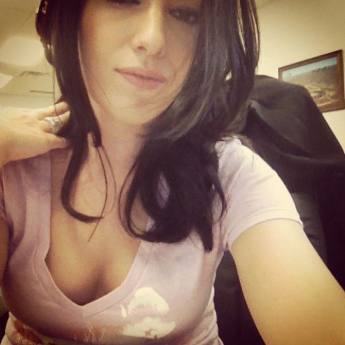 pretty lady with pink lips shows off her cleavage in purple top while sitting on office chair.