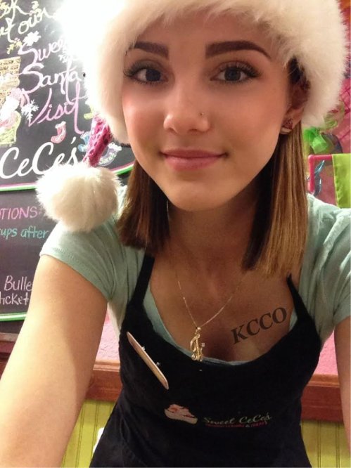 Blonde with perky boobs takes selfie in Santa hat, blue top, and black apron