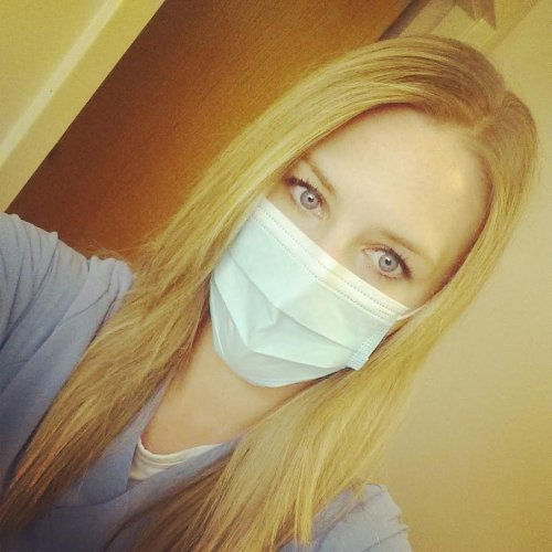 Light-eyed blonde takes selfie in white face mask and grey top