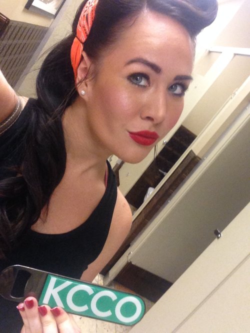 Brunette with red lips and KCCO bottle opener takes selfie in black top