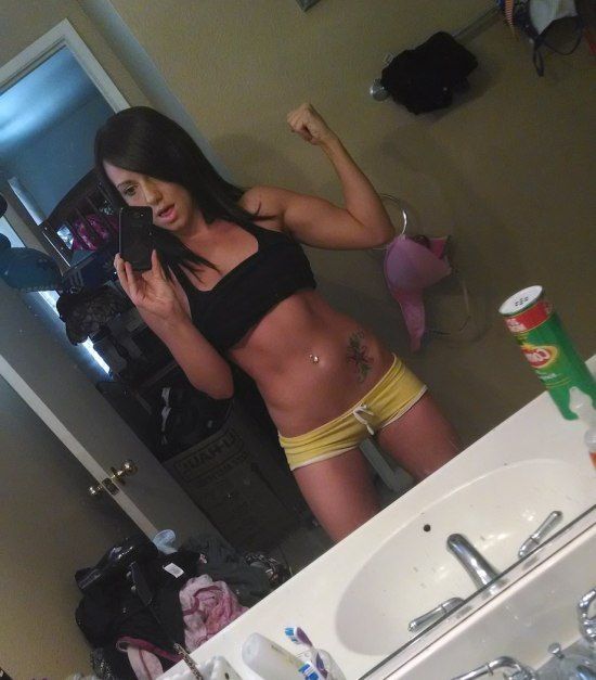 Pretty tattooed brunette with perky boobs, flat abs, slender legs, and slim sexy hot body takes selfie in black top and yellow shorts