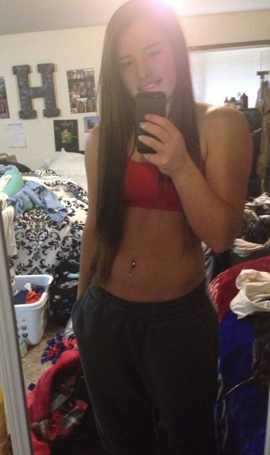 Brunette with perky boobs, flat abs, flowing tresses, and sexy hot body takes selfie in red sports bra and black sweat pants