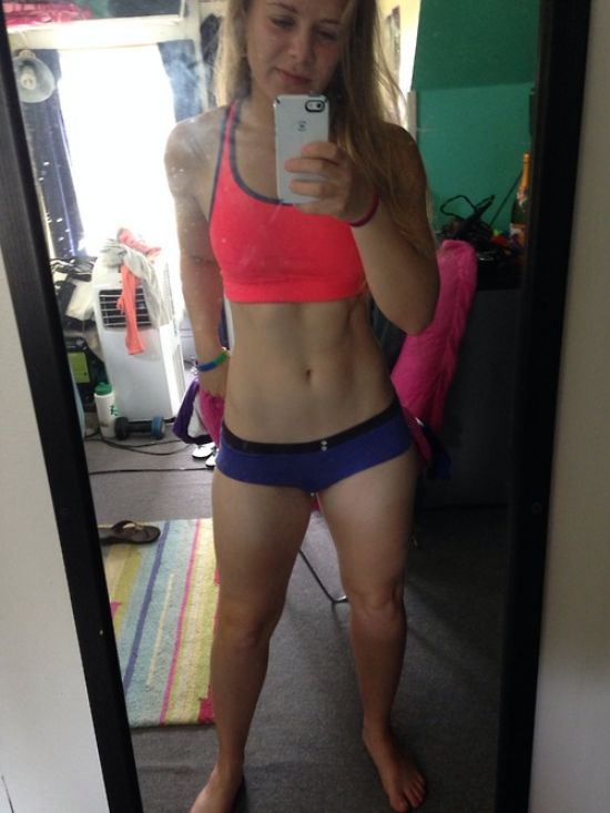 Blonde with flat abs, slender legs, perky boobs, and slim sexy hot body takes selfie in pink sports bra and purple panties