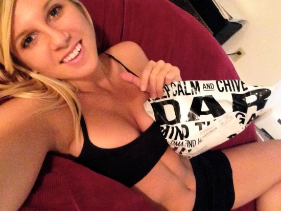 blonde in black sports bra and spandex shorts on red couch holding chive package