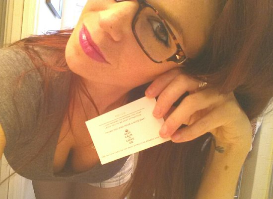 Girl bending over showing cleavage in glasses and pink lipstick holding a business card