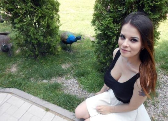 girl with arm tattoo wearing black tank top and white skirt taking picture with a peacock
