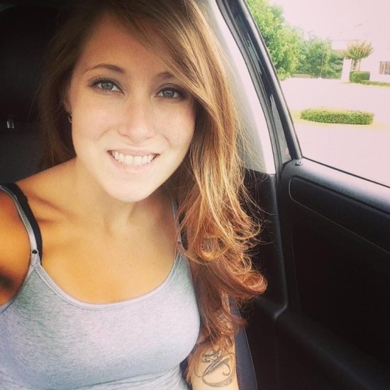 girl taking selfie in car with tattoos on arm and grey tank top