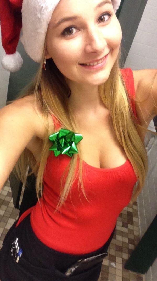 Pretty light-eyed blonde with perky juicy boobs and slim sexy curvy hot body takes selfie in red Santa hat, cleavage showing red top, and black pants