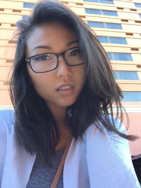 Pretty Asian brunette takes selfie in glasses, grey top, and white cardigan