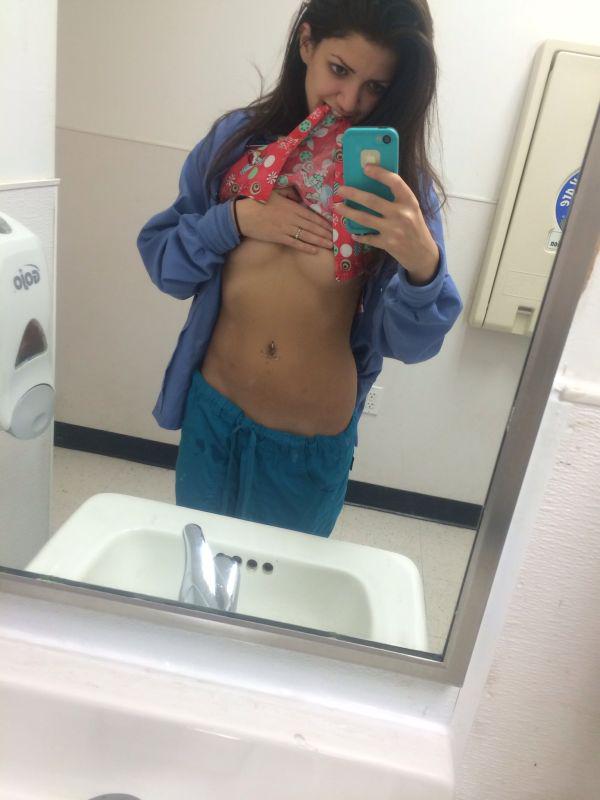 Pretty brunette with flat abs and sexy body in blue pants and purple jacket lifts red top and takes selfie of underboobs