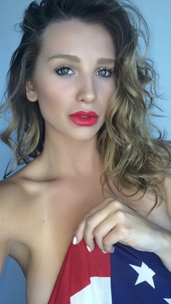Light-eyed blonde with red juicy lips covers naked juicy boobs with American flag and takes selfie