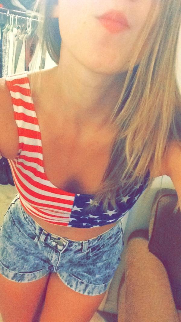 Blonde with red full lips and slim sexy body takes selfie in blue denim shorts and stars and stripes crop top