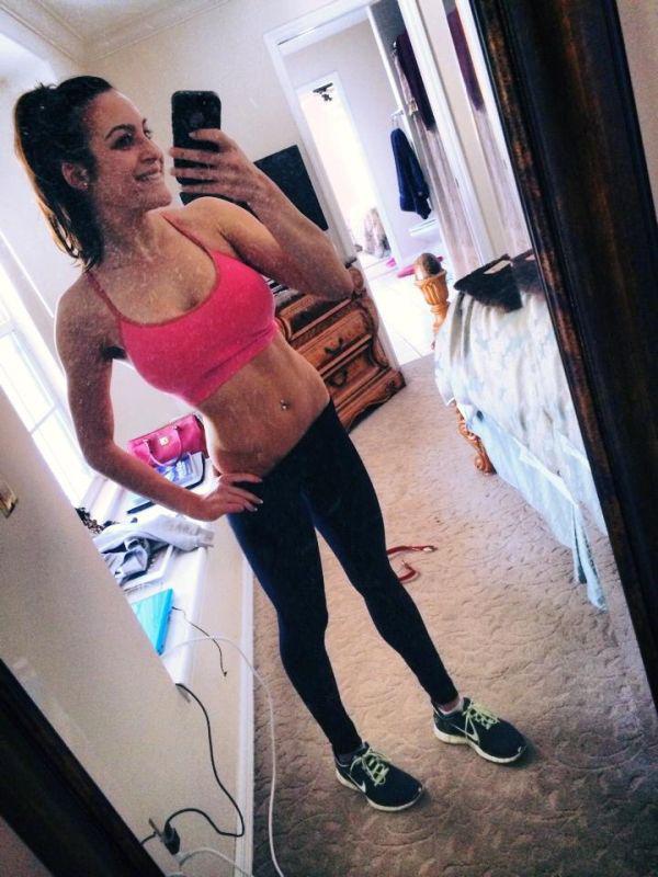 Hot brunette takes a selfie wearing pink to and black track pants, at the gym