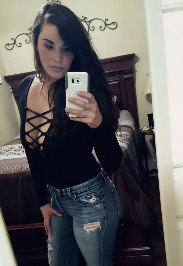 Sexy brunette with long hair, takes a selfie in a netted black top and denim jeans.