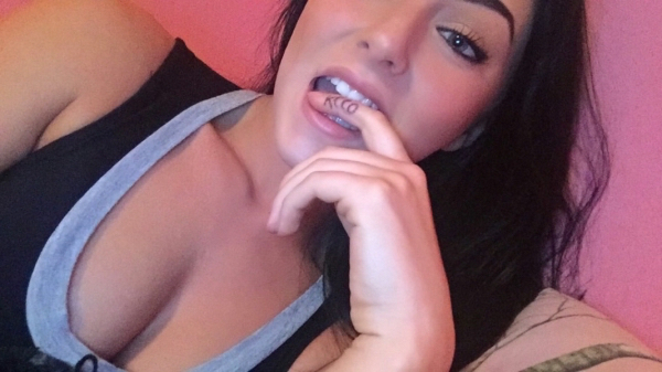 Beautiful babe sticks her index finger with'KCCO' written on it, in her mouth.