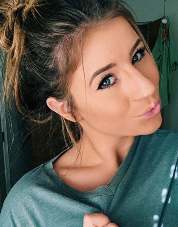 Bubbly girl taking a happy pout selfie with messy high hair bun and shining green eyes