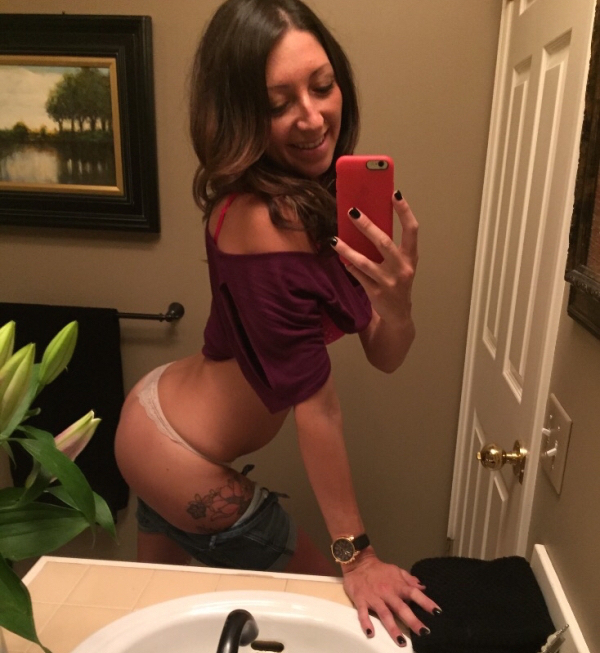 Hot brunette pushing out her booty to take a selfie in the washroom mirror