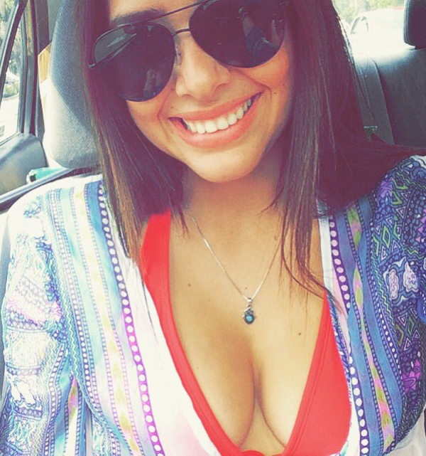 Sexy MILF smiles beautifully, showing off her black shades, beautiful pendant and large cleavage through her red bra.