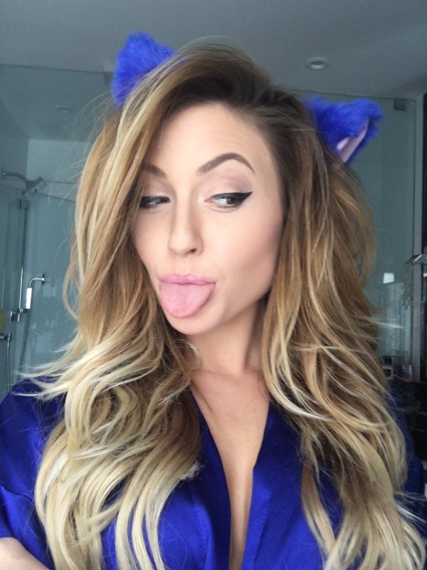 Gorgeous girl with deep cleveage in stylish royal blue top andblue fur bow on head sticking out her tongue and streched eyebrows to make a funny face