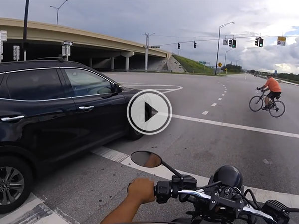 A cyclist crossing the road in front of a motorbike and car.