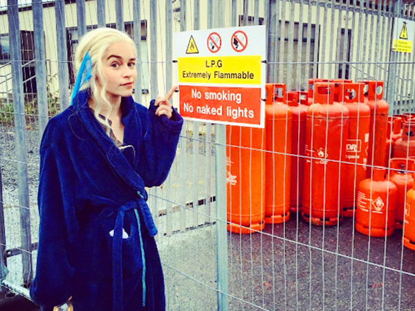 Emilia Clarke in blue bathrobe pointing to a danger sign