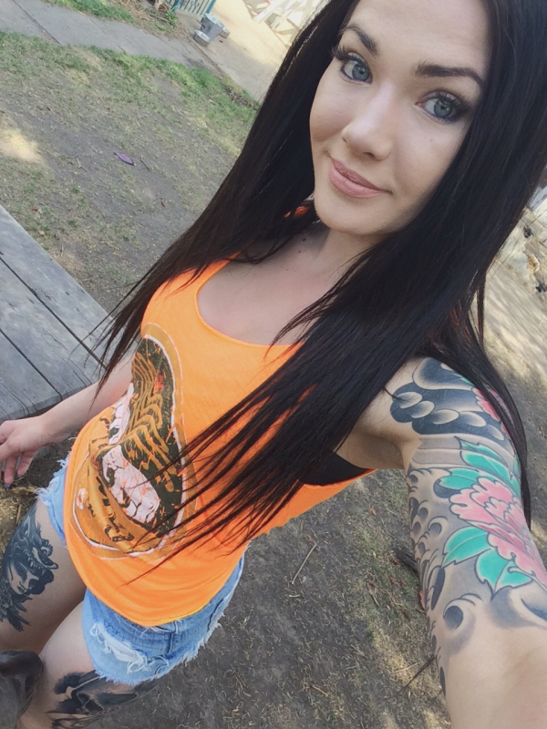 Tattooed girl with green eyes wearing an orange top and short blue denims