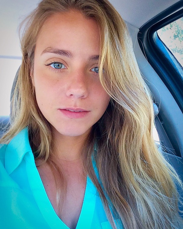 Cute blonde with light eyes takes selfie in car in blue top