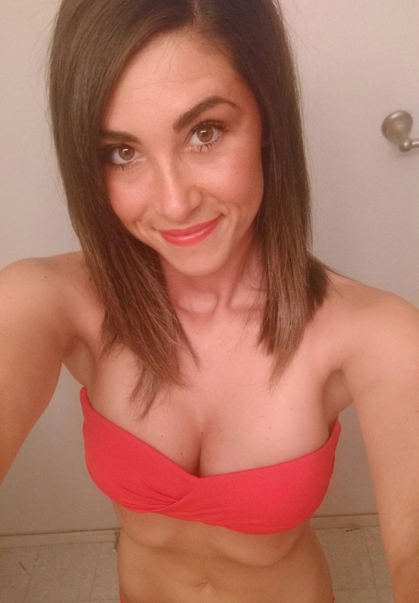Brunette with light eyes and perky boobs takes selfie of slim body in cleavage showing red bikini top