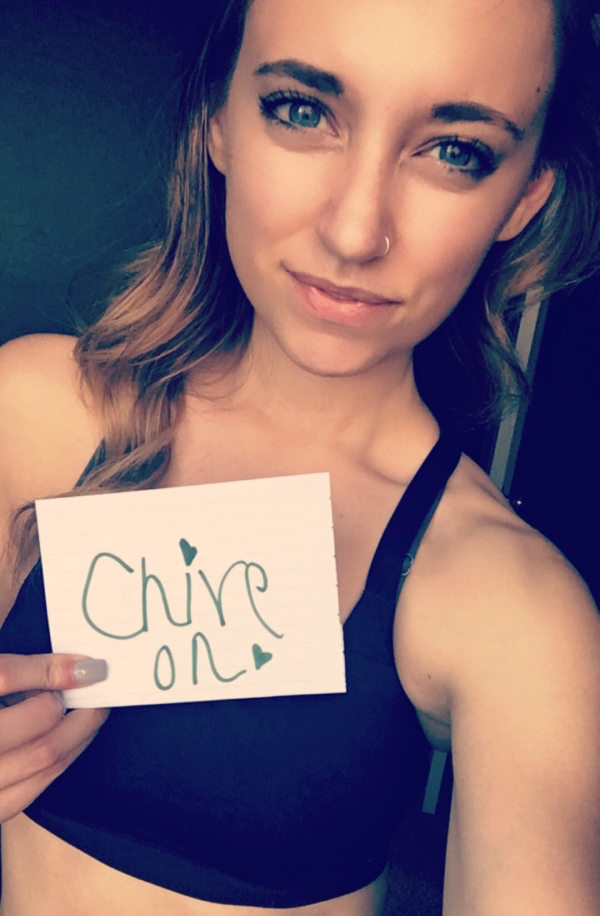 Green eyed girl with a nose ring holds a 'Chive On!' sign in her hand