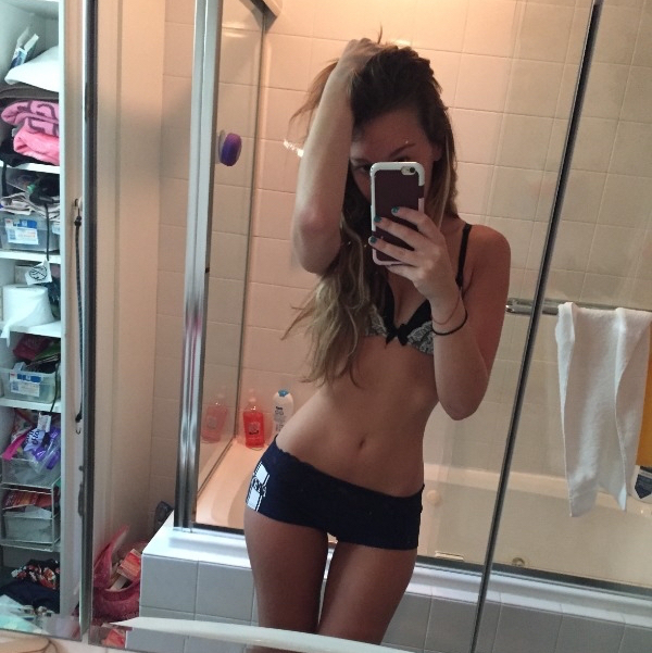 Skinny girl clicks a mirror selfie in her bathroom wearing short black pants and black bra