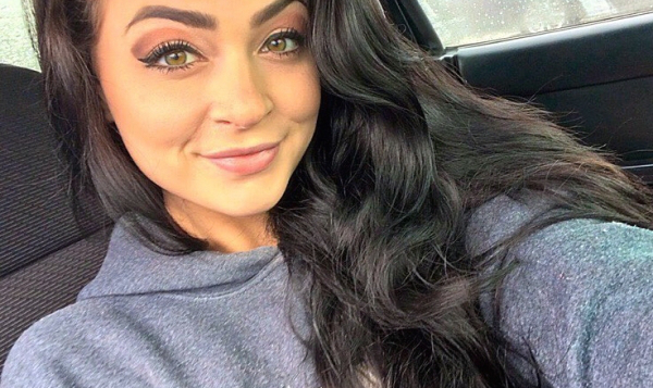 Brunette with cat eyes and flowing tresses takes selfie in grey hoodie