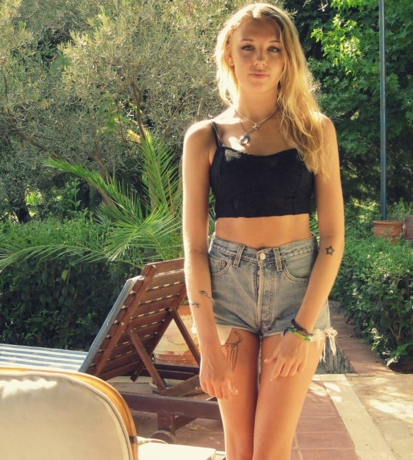 Blonde girl wearing a black top and short denims stands in the porch for a picture