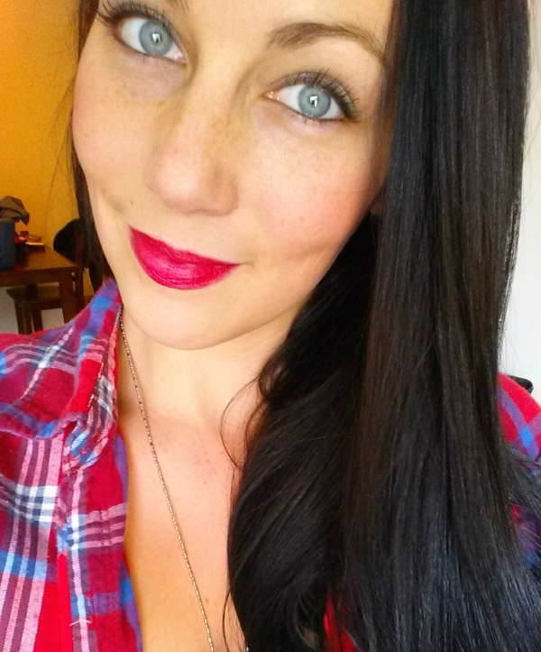 Brunette with bright red lips and light eyes takes selfie in red checked shirt