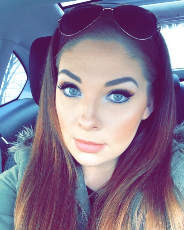 Brunette with plump lips and light eyes takes selfie in car in grey jacket