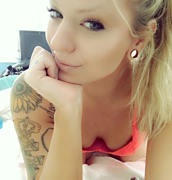 Tattooed girl clicks a close-up selfie wearing a pink top with cleavage visibe