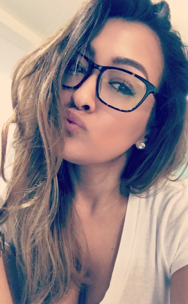Cute spectacled girl pouts for the picture with her cleavage visible through the white top