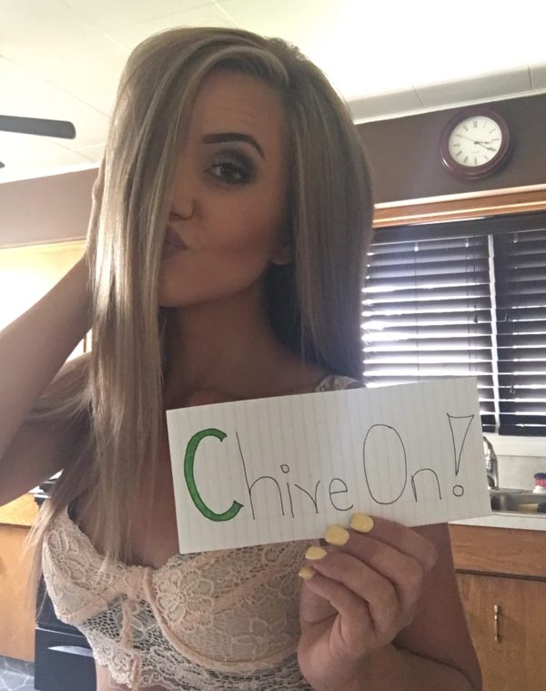 Girl pouts for the picture with a 'Chive On!' sign in her hand wearing a cream colored bra
