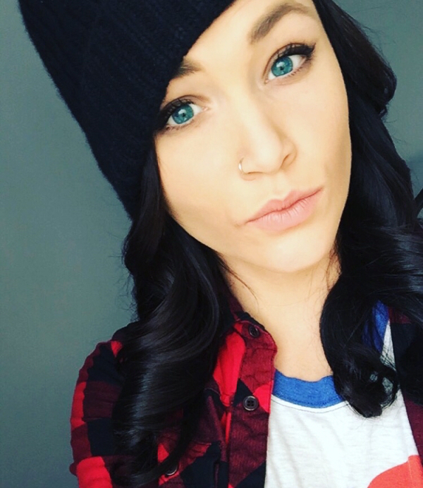 Brunette with green eyes takes selfie in black beanie cap, red shirt, and white tee